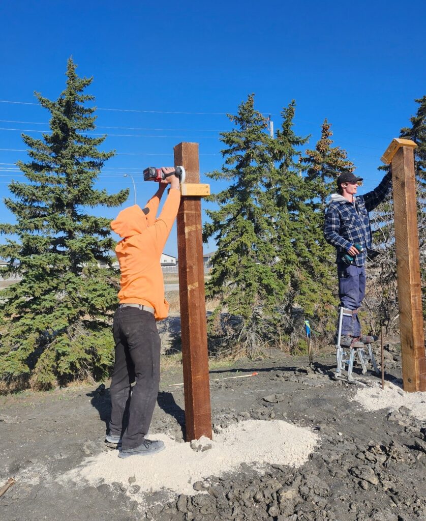 Two people constructing wooden posts.
